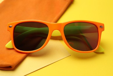 Photo of Stylish sunglasses with bag on yellow background, closeup
