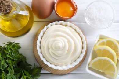 Photo of Fresh mayonnaise sauce in bowl and ingredients on white wooden table, flat lay