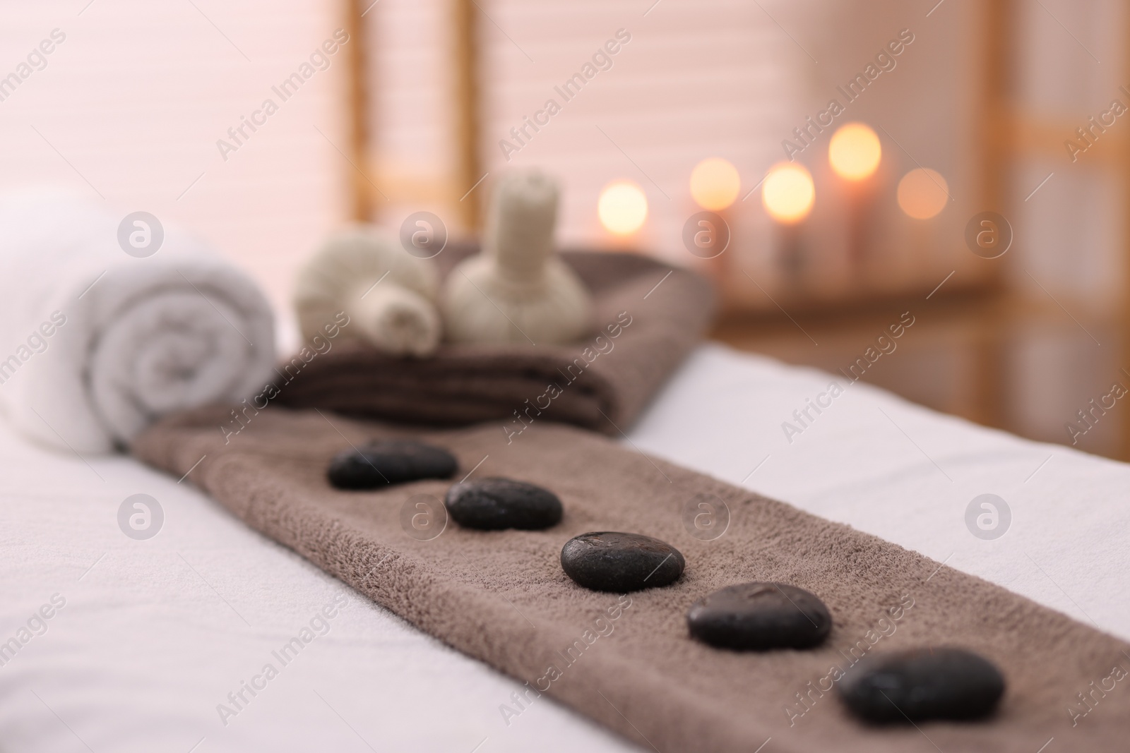 Photo of Towel with arranged spa stones on massage table in recreational center, closeup