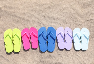 Many stylish colorful flip flops on sand outdoors, flat lay