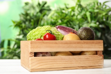 Fresh vegetables in crate on white wooden table against blurred green background