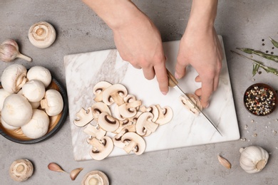 Photo of Young woman cutting fresh champignon mushrooms on marble board, top view
