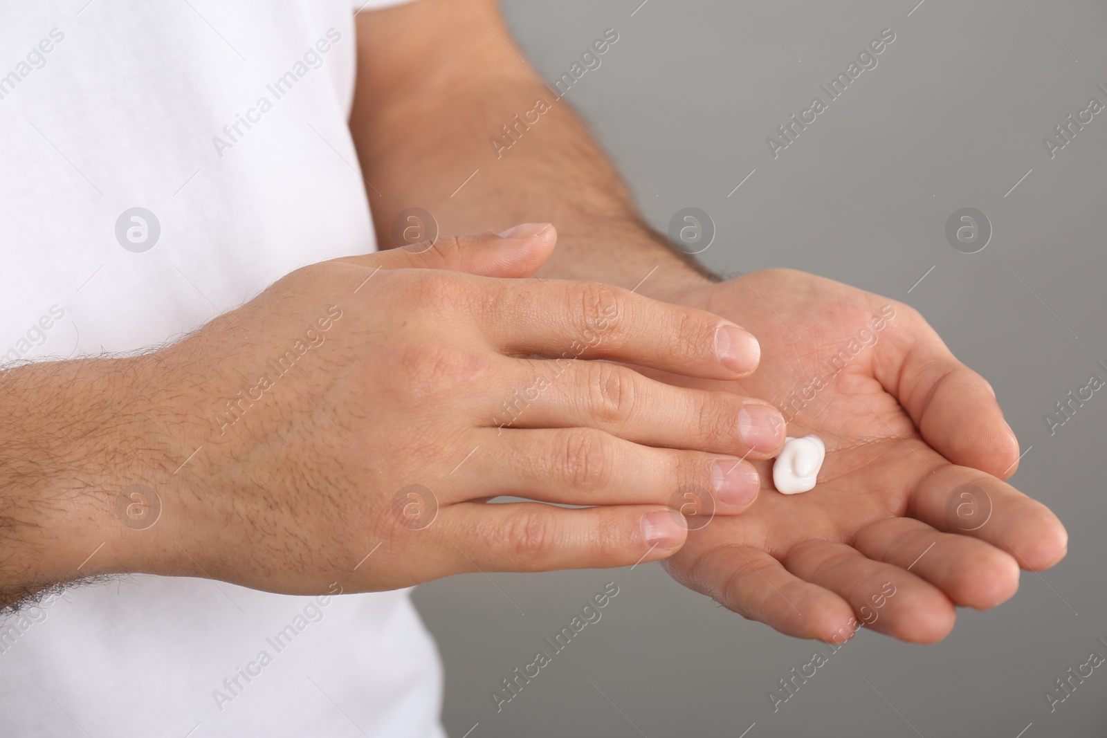 Photo of Man applying cream onto hand on grey background, closeup