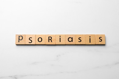 Photo of Word Psoriasis made of wooden squares with letters on white marble table, top view