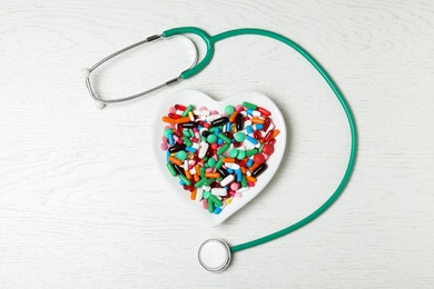 Photo of Plate with heart pills and stethoscope on wooden background, flat lay. Cardiology concept