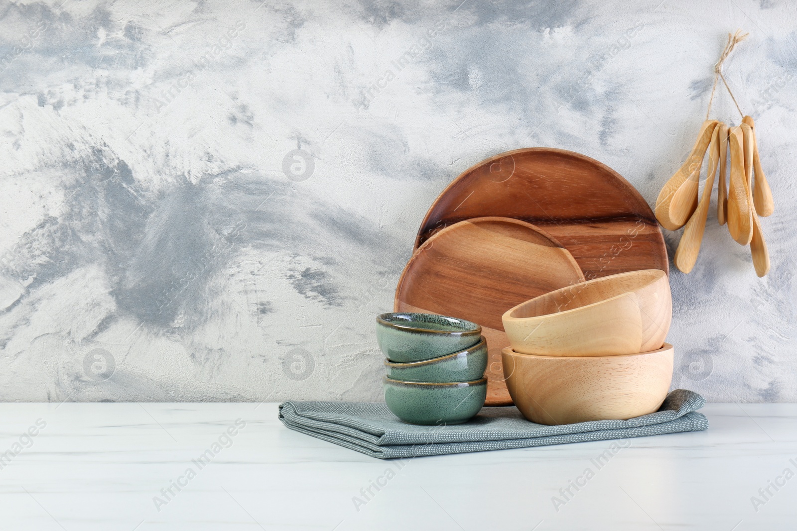 Photo of Different dishware and utensils on white marble table against textured wall. Space for text