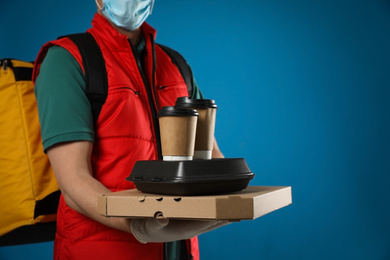 Courier in protective mask and gloves holding order on blue background, closeup. Food delivery service during coronavirus quarantine