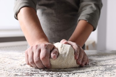 Man kneading dough at table in kitchen, closeup