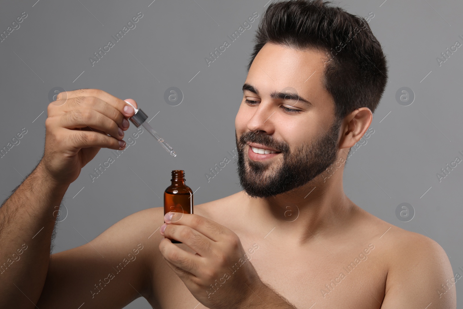 Photo of Handsome man with cosmetic serum in hands on grey background