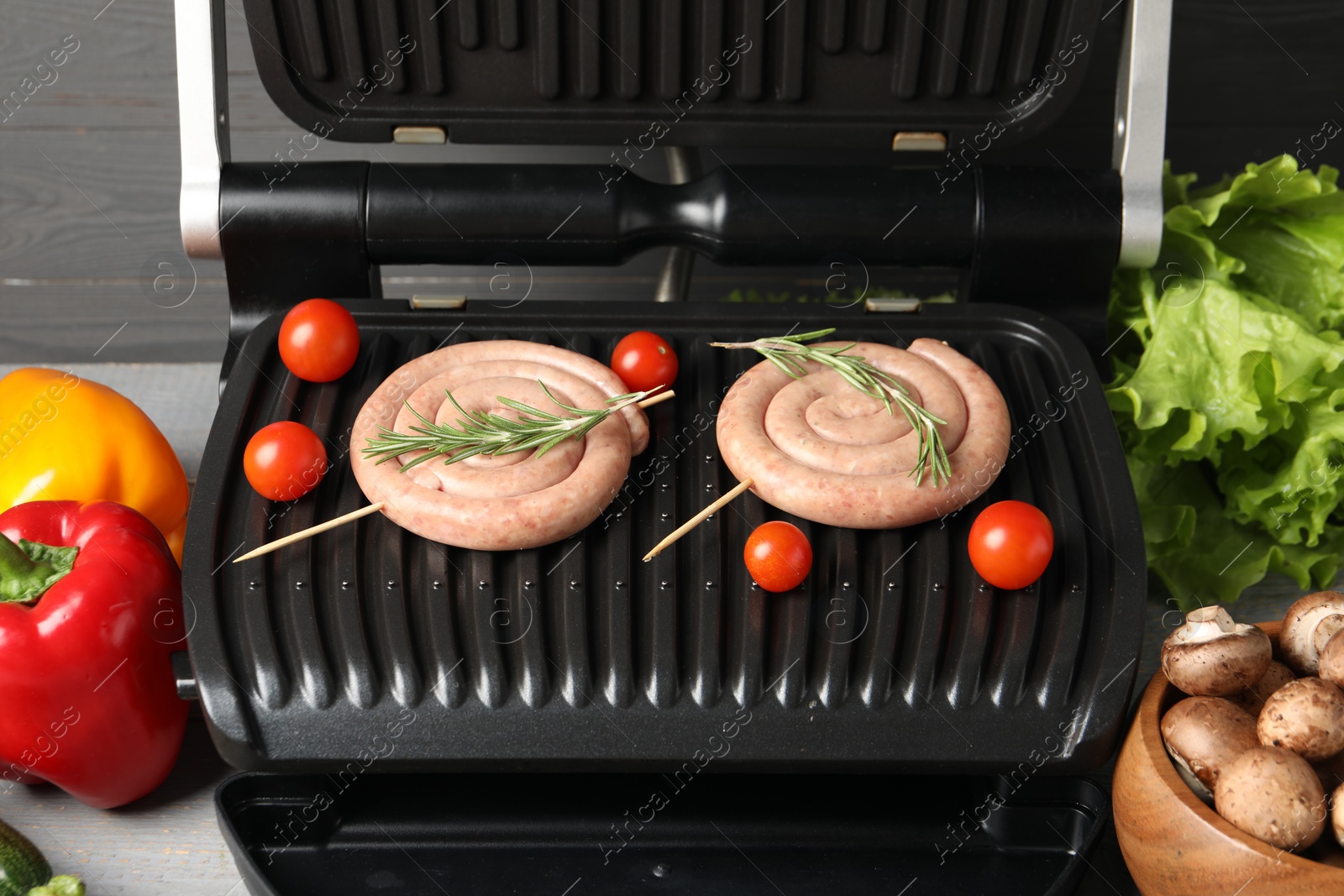 Photo of Electric grill with homemade sausages, rosemary and vegetables on table