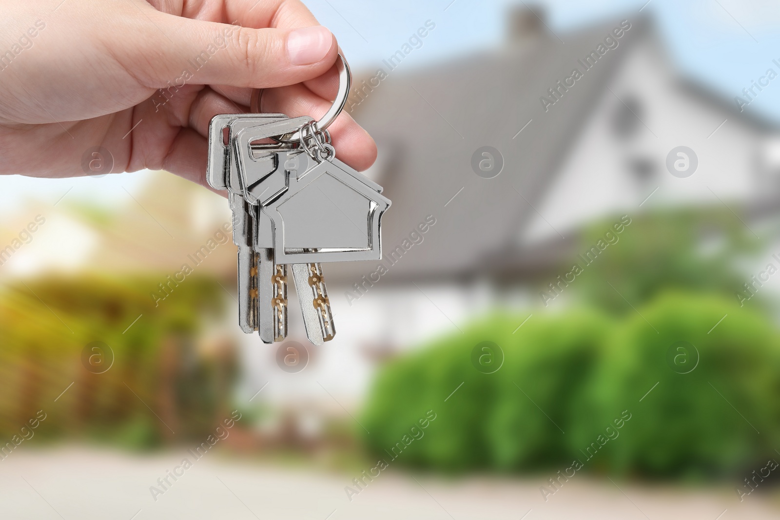 Image of Woman holding keys near house outdoors, closeup