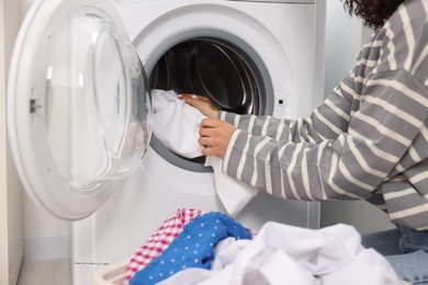 Woman putting laundry into washing machine indoors, closeup