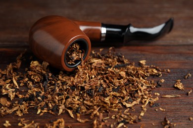 Photo of Smoking pipe and dry tobacco on wooden table, closeup