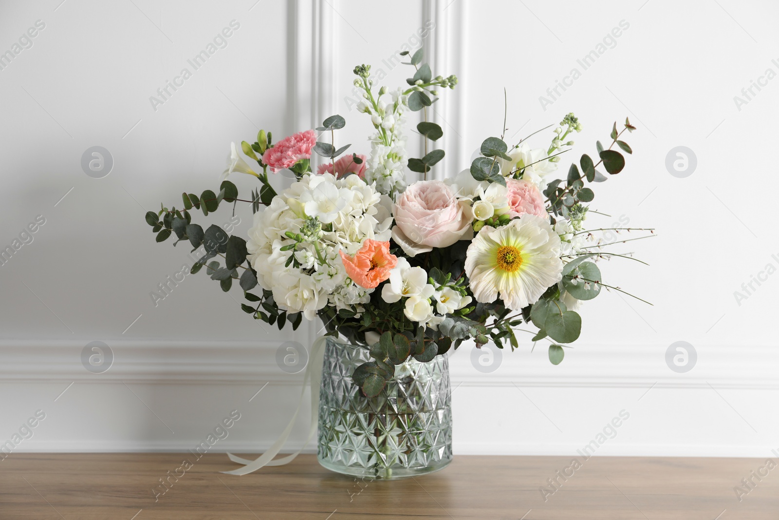 Photo of Bouquet of beautiful flowers in vase on wooden table near white wall