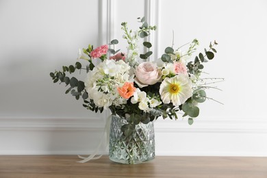 Bouquet of beautiful flowers in vase on wooden table near white wall