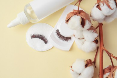Bottle of makeup remover, cotton flowers, pad and false eyelashes on yellow background, flat lay. Space for text