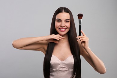 Happy woman with makeup brush on light grey background