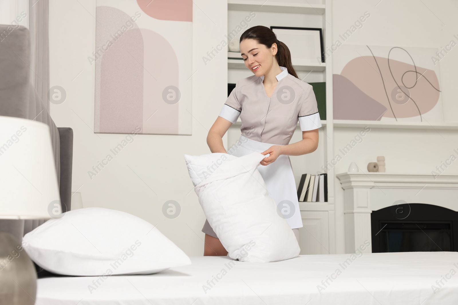 Photo of Young maid making bed in hotel room