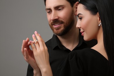 Man putting elegant ring on woman's finger against dark grey background, closeup