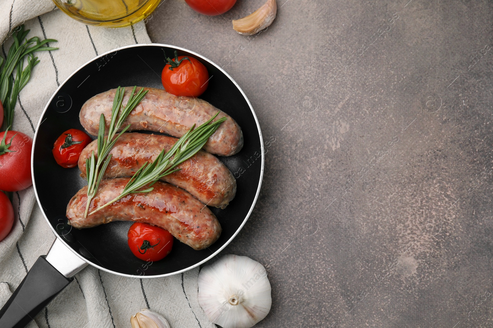 Photo of Frying pan with tasty homemade sausages, rosemary and tomatoes on brown textured table, flat lay. Space for text