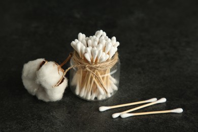 Photo of Cotton swabs and flower on black table, space for text