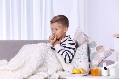 Photo of Ill boy suffering from cough on sofa at home