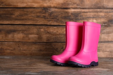 Photo of Pair of bright pink rubber boots on wooden surface. Space for text