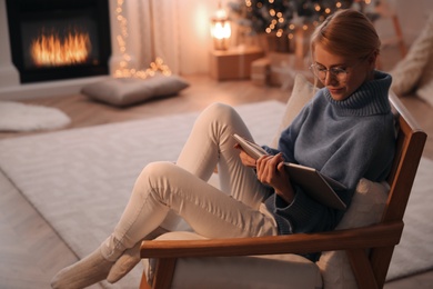 Young woman reading book at home, space for text. Christmas celebration