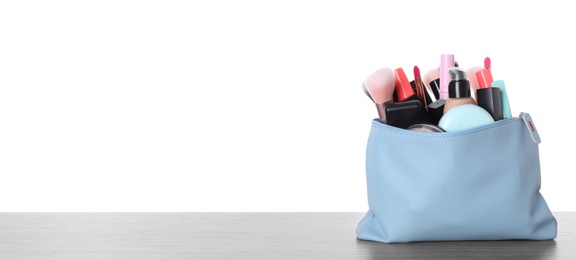 Bag with makeup brushes and cosmetic products on grey table against white background. Space for text