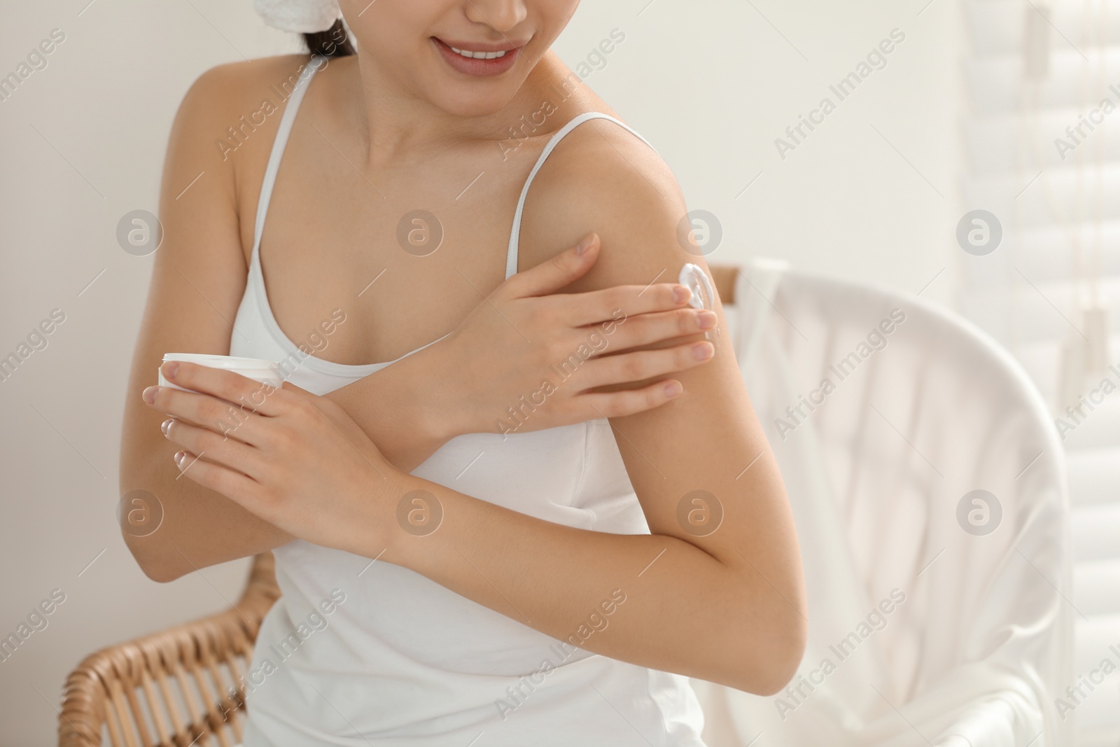 Photo of Young woman applying body cream on shoulder in room, closeup. Space for text