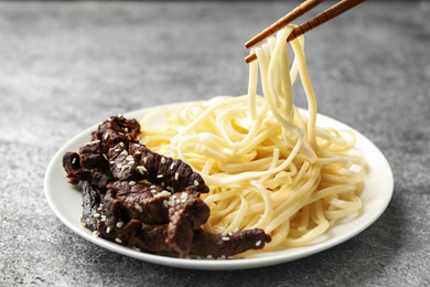 Chopsticks with tasty cooked rice noodles over plate on grey table