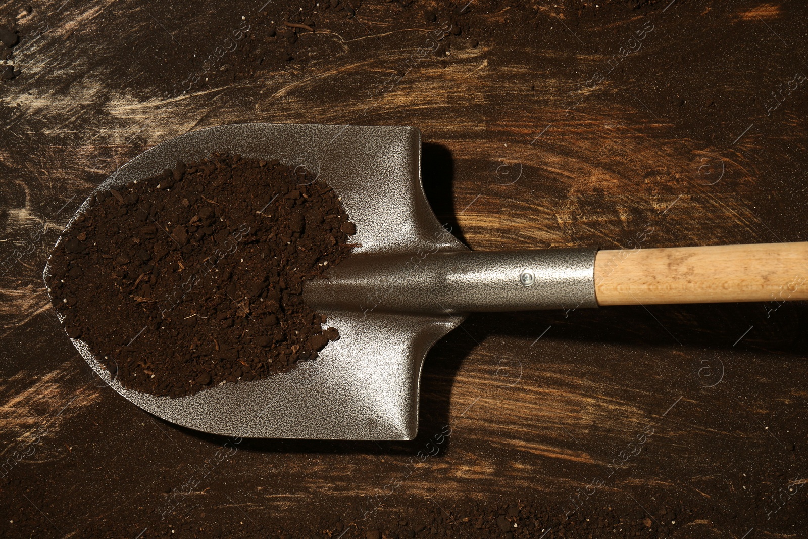 Metal shovel with fertile soil on dirty wooden surface, top view Photo of Metal shovel with fertile soil on dirty wooden surface, top view