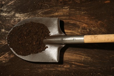Photo of Metal shovel with fertile soil on dirty wooden surface, top view