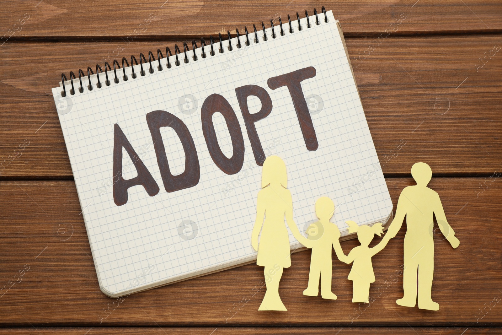 Photo of Family figure and notebook with word Adopt on wooden table, flat lay