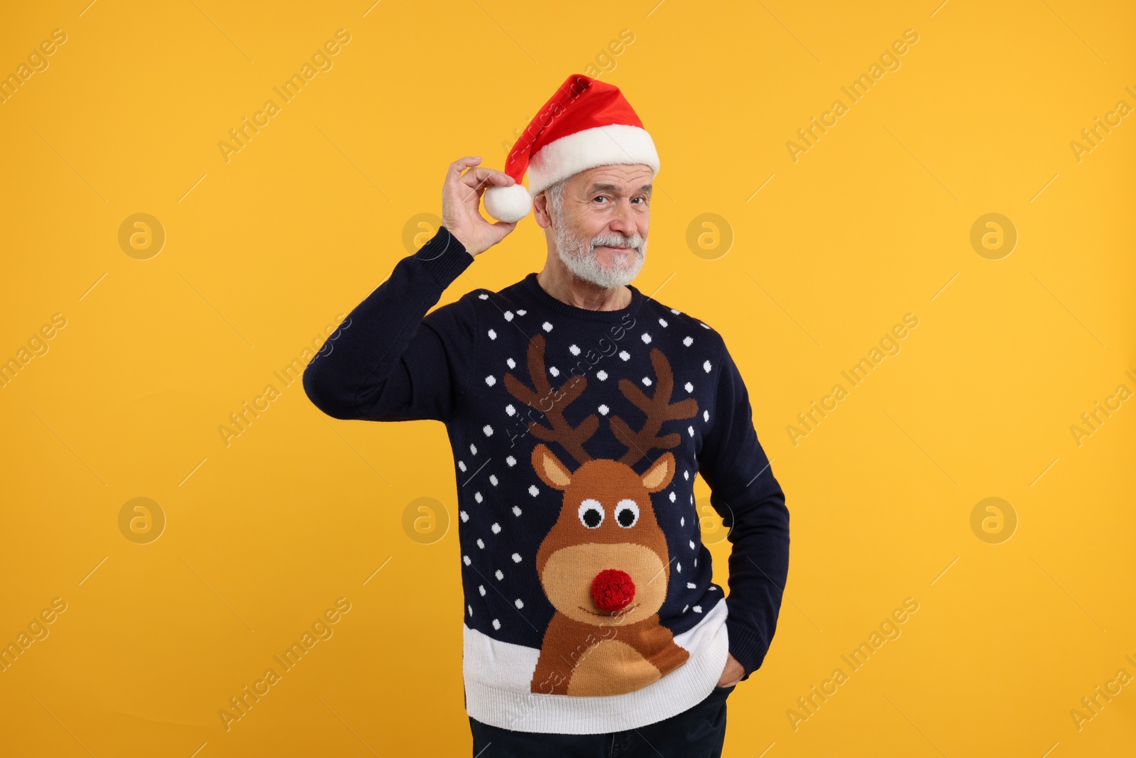 Photo of Senior man in Christmas sweater and Santa hat on orange background