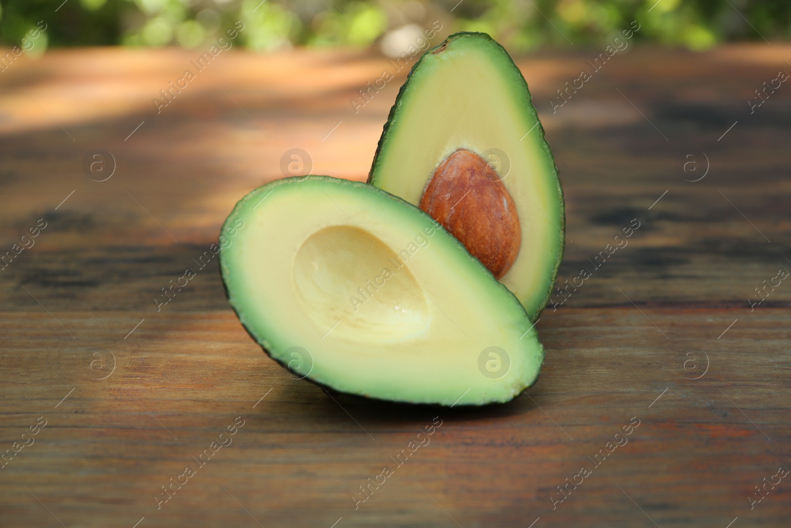 Photo of Halves of fresh avocado on wooden table outdoors