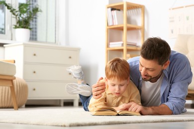 Photo of Father reading book with his son on floor in living room at home