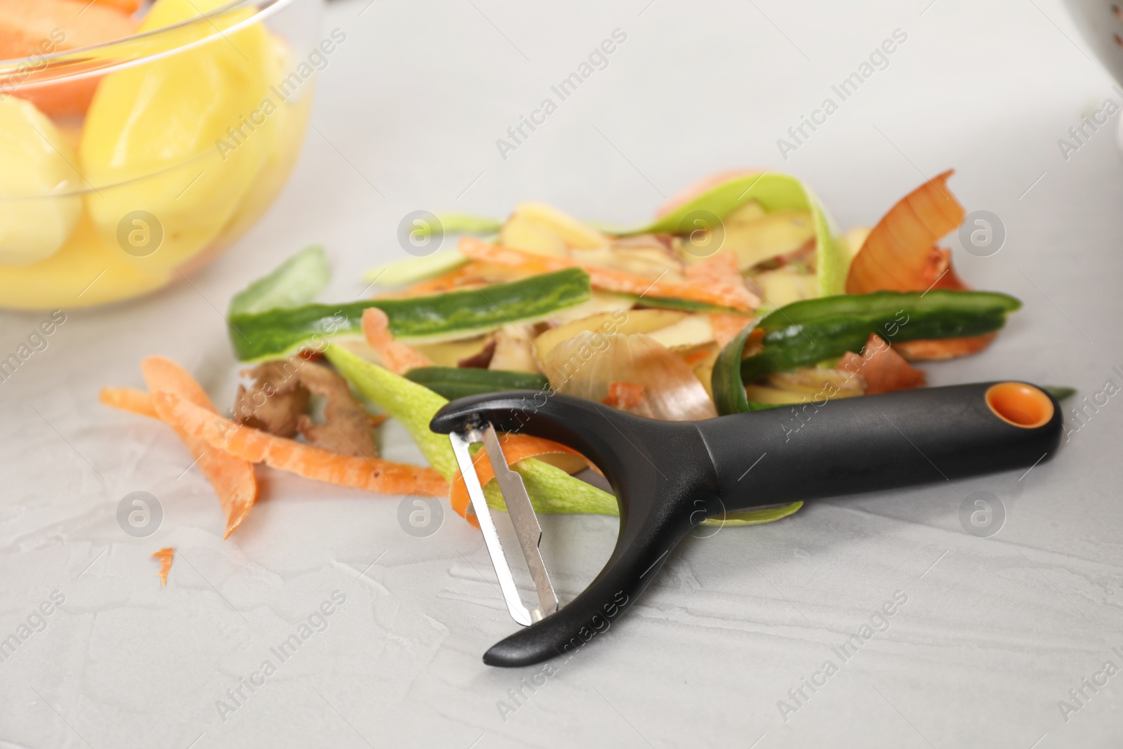 Photo of Peels of fresh vegetables and peeler on white table, closeup