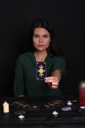 Photo of Soothsayer predicting future at table against black background, closeup. Focus on tarot card