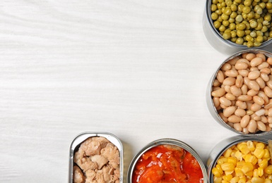 Open tin cans with different vegetables and fish meat on light table, flat lay. Space for text