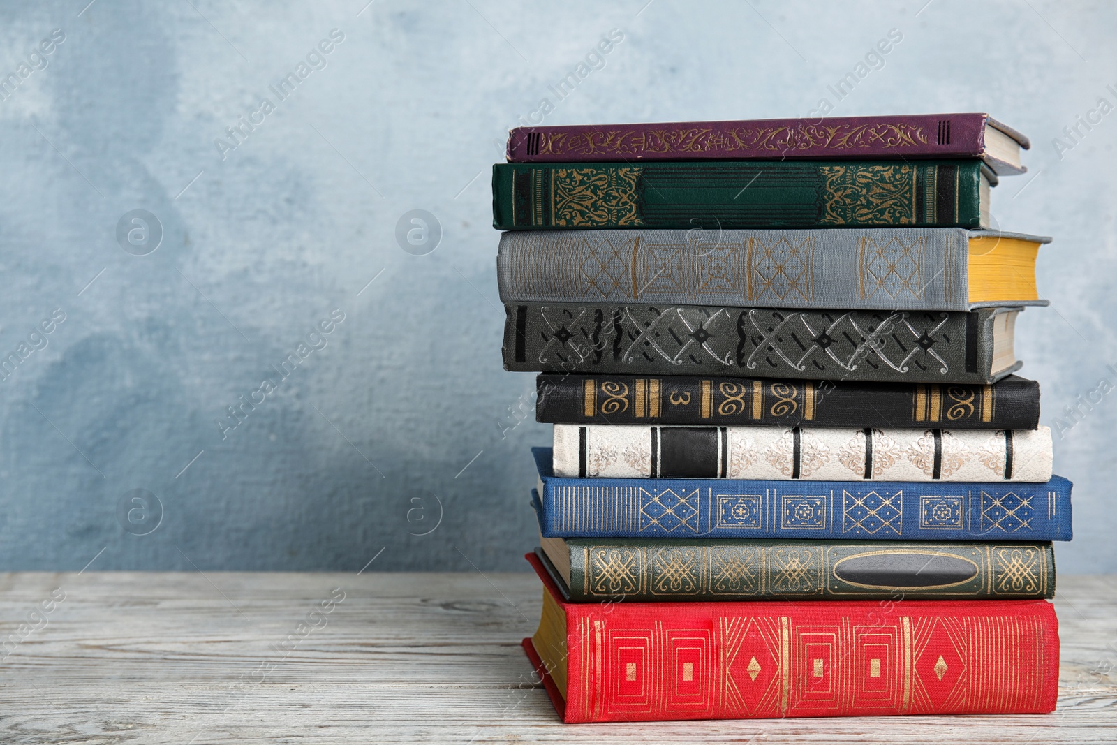 Photo of Stack of hardcover books on wooden table against light blue background. Space for text