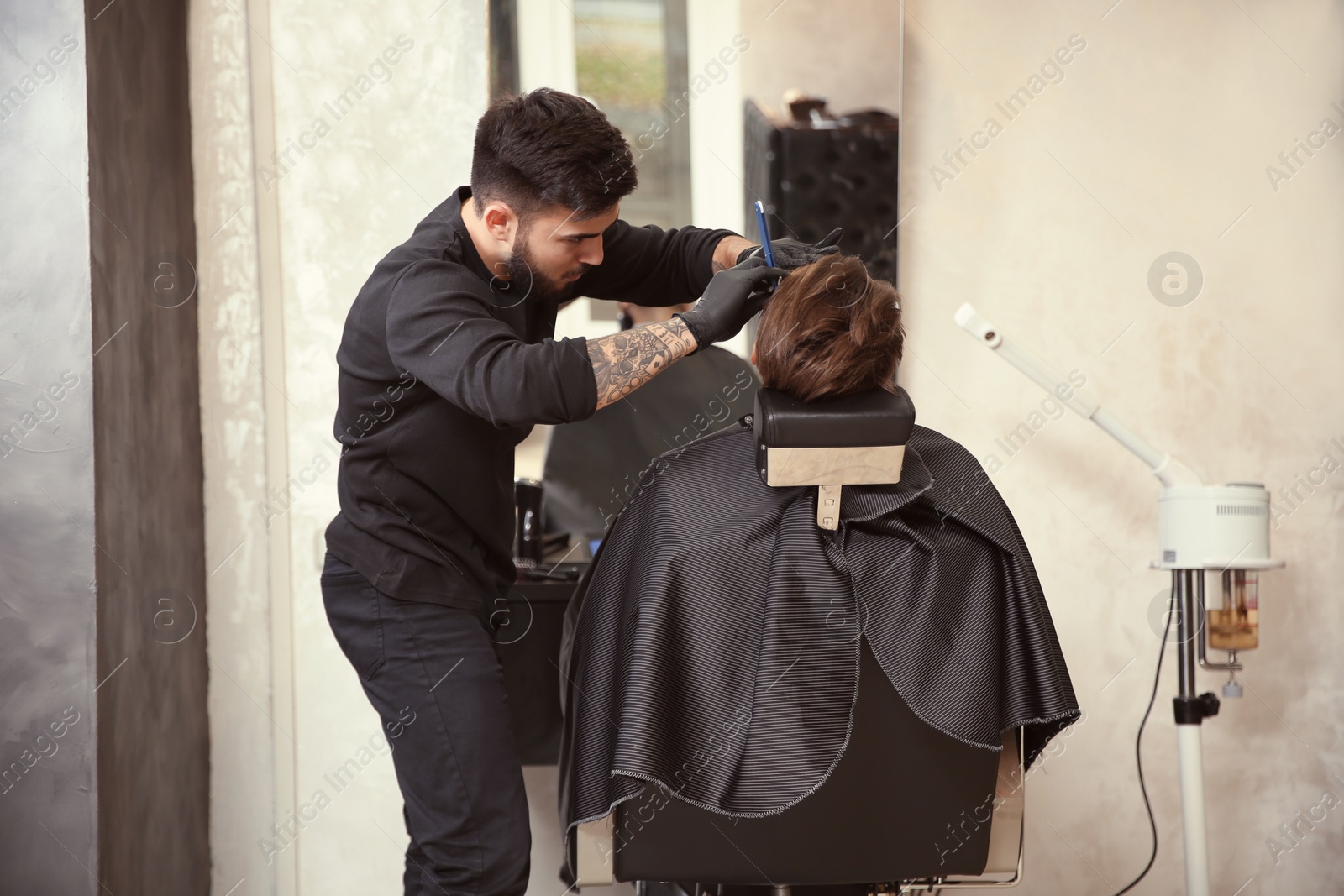 Photo of Professional hairdresser shaving client with straight razor in barbershop