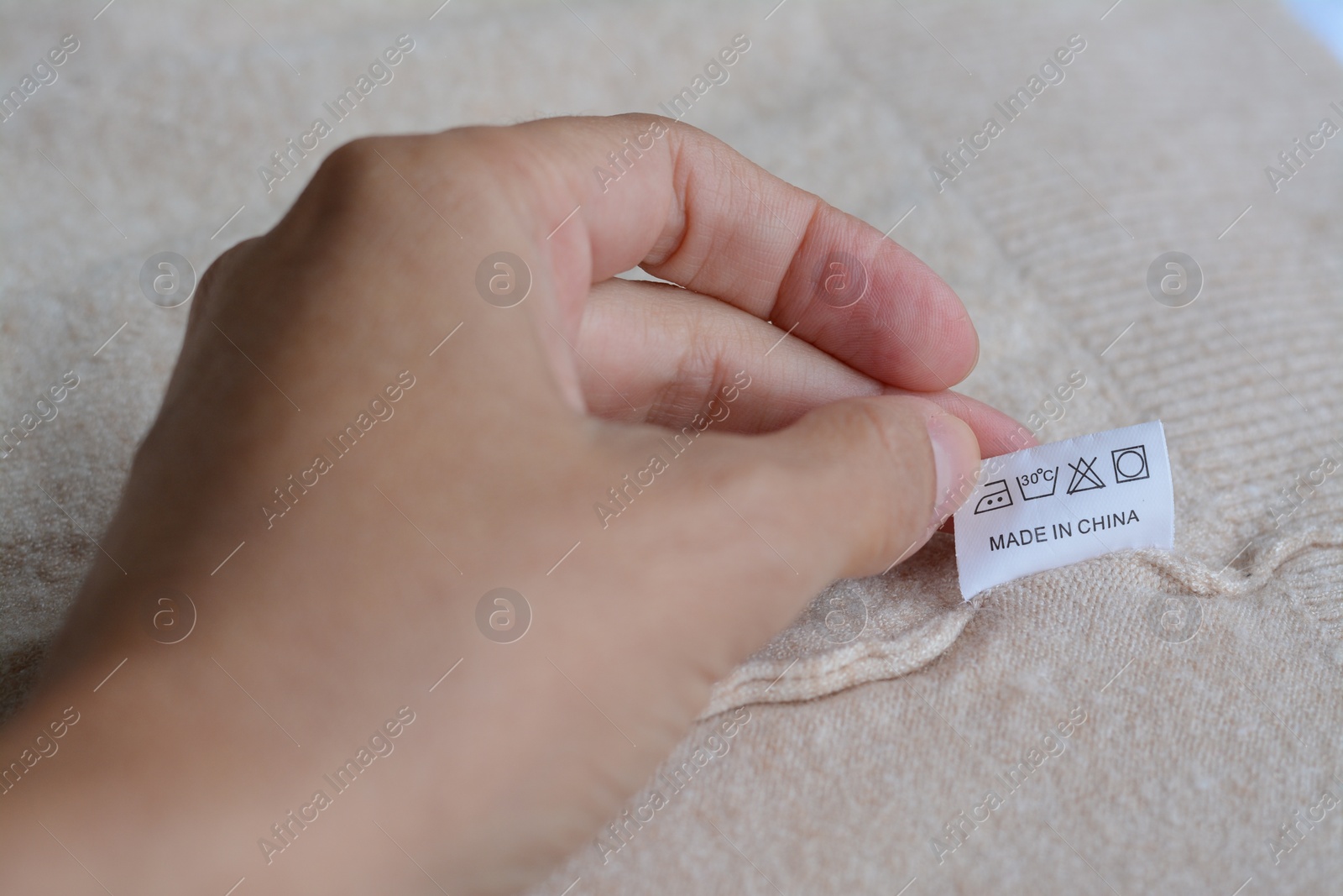 Photo of Woman holding white clothing label on beige garment, closeup