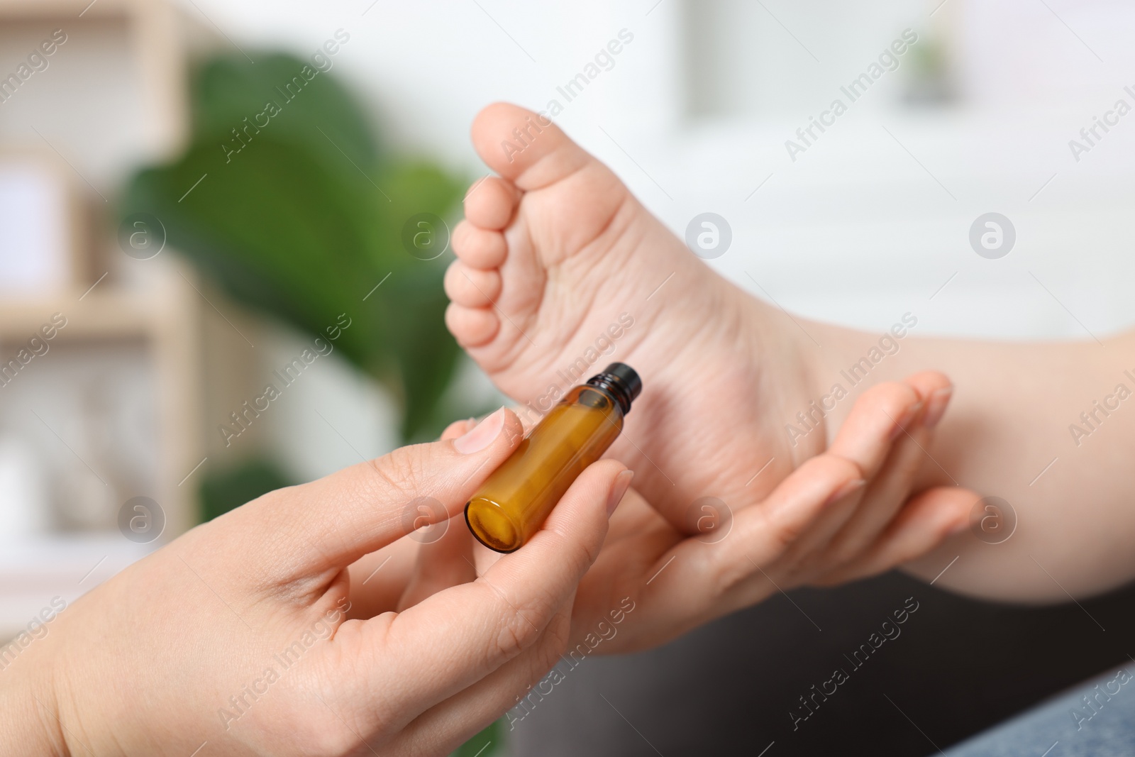 Photo of Mother applying essential oil from roller bottle onto her baby`s heel indoors, closeup