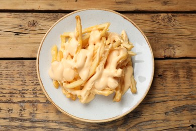 Photo of Delicious French fries with cheese sauce on wooden table, top view