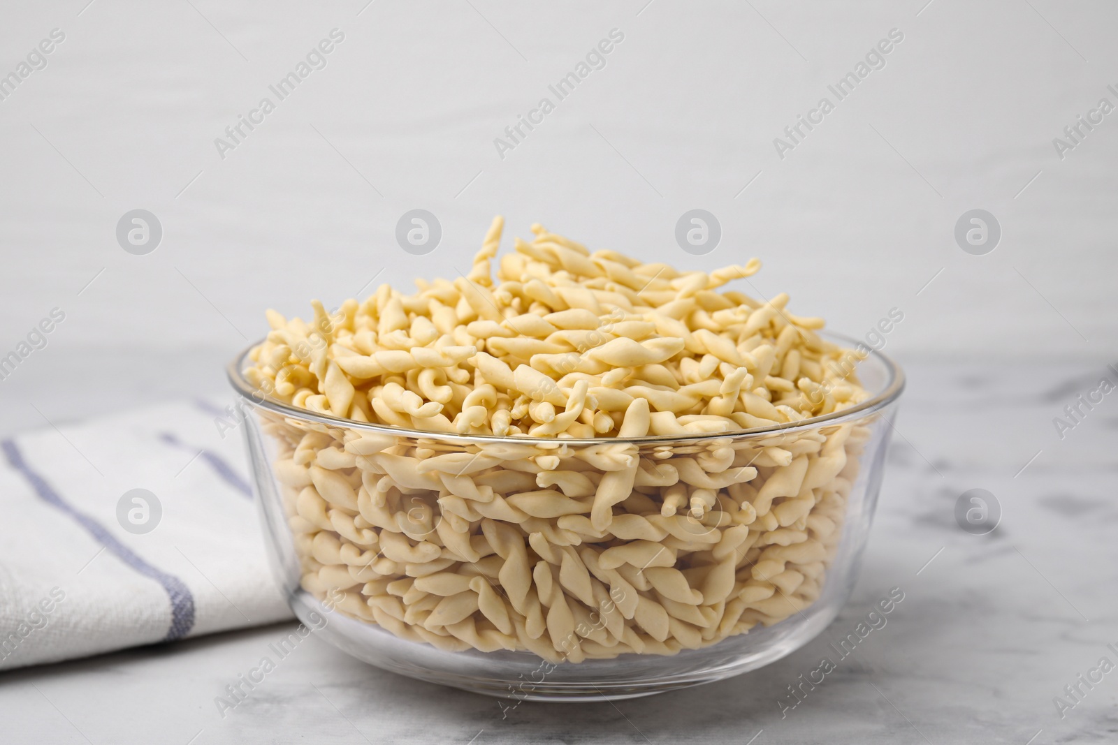 Photo of Uncooked trofie pasta in bowl on white marble table, closeup