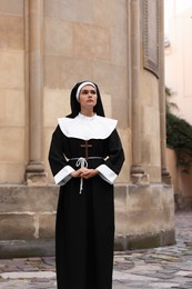 Photo of Young nun with Christian cross near building outdoors