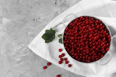 Photo of Ripe red currants in colander and leaves on grey textured table, flat lay. Space for text