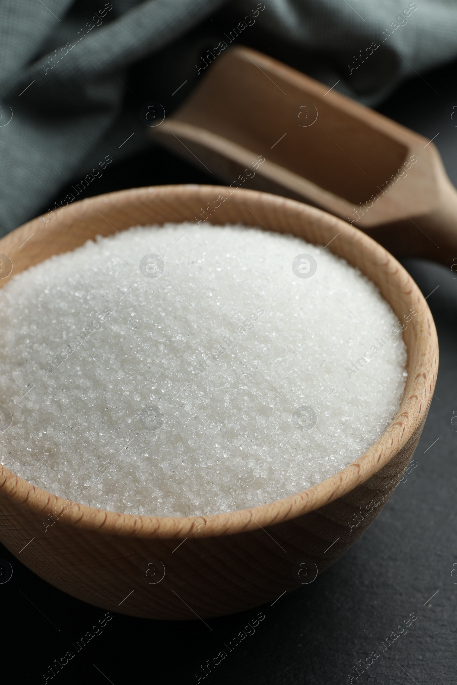 Photo of Granulated sugar in bowl on black table, closeup