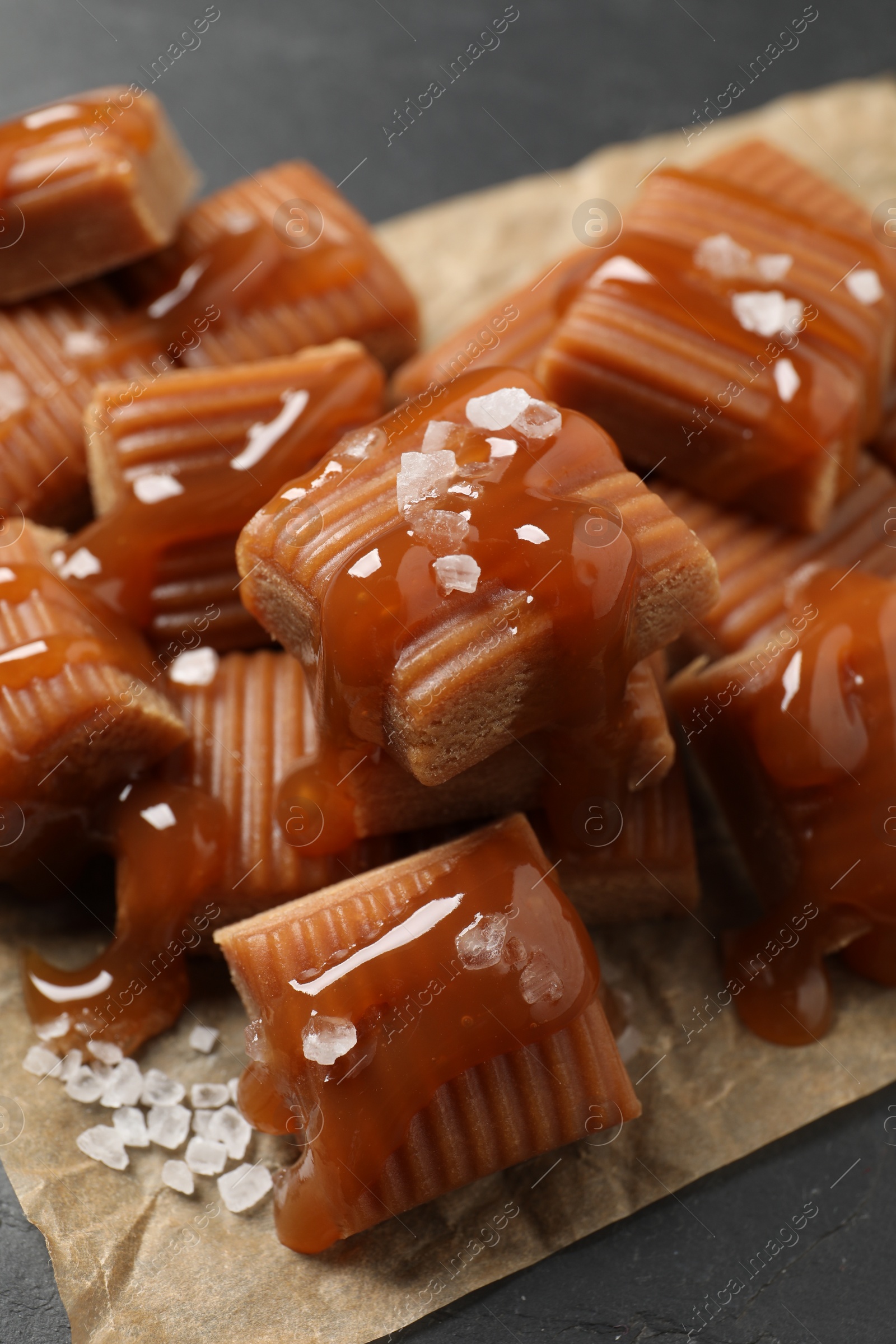 Photo of Tasty caramel candies with sauce and sea salt on grey table, closeup